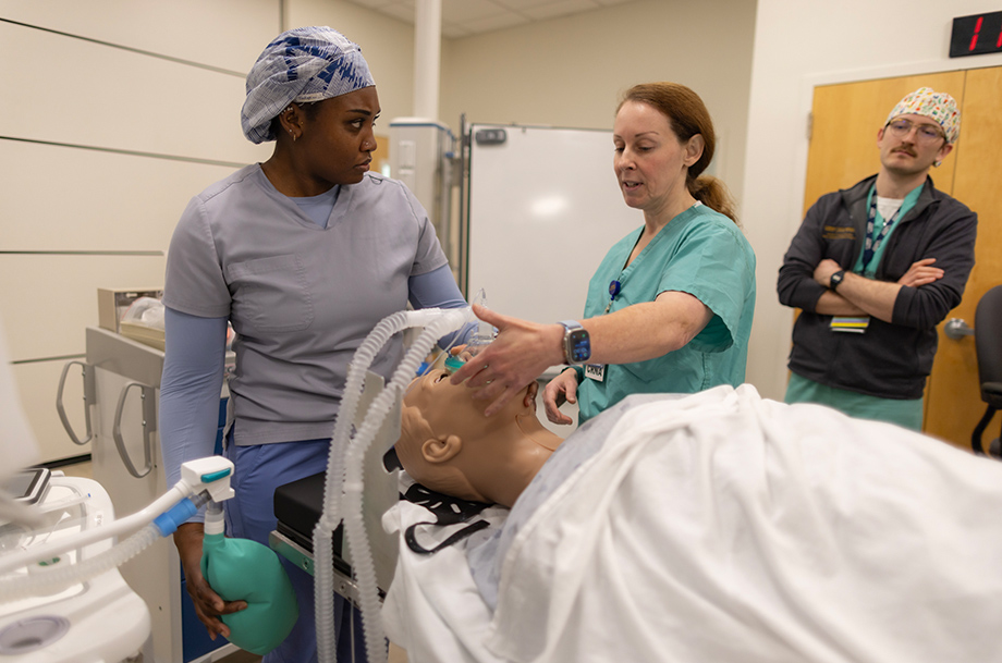 Faculty member demonstrates airway management on a mannikin while students observe during a hands-on clinical training session.