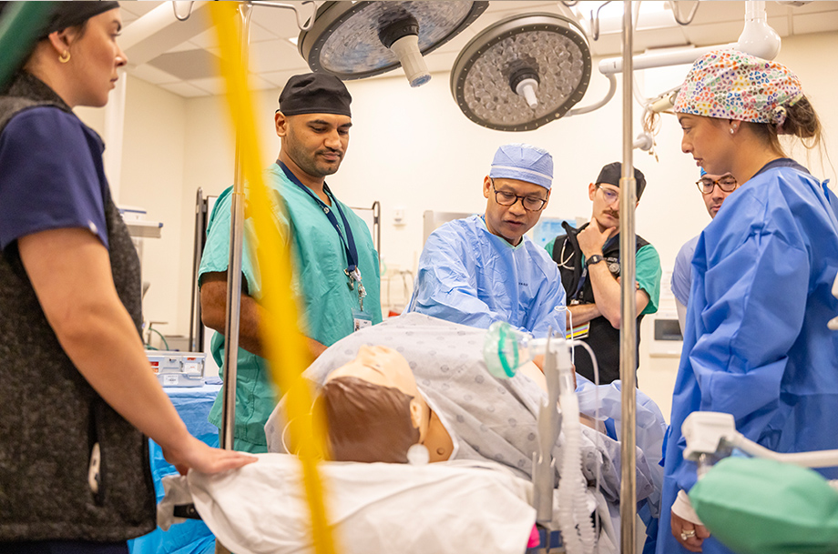 Faculty and students gather around a mannikin in an operating room simulation during a hands-on training session.