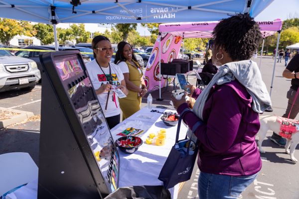 Three people talking at an information booth under a tent at a community event.  