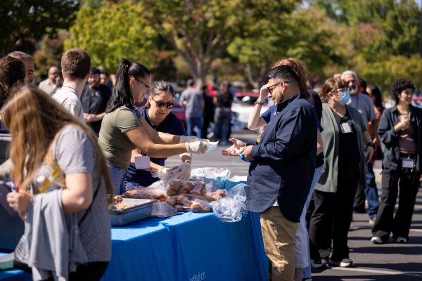 Volunteers at car show serve free food from table in parking lot. 