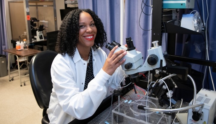 Researcher Theanne Griffith sits using a microscope-like instrument surrounded by scientific equipment.