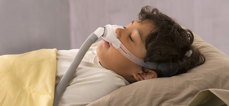 A child in bed wears a CPAP