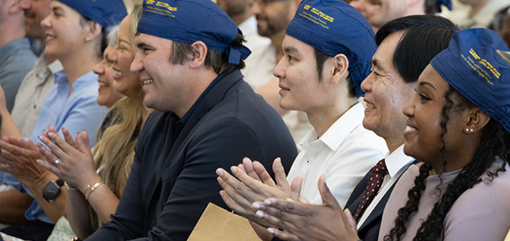 Nurse anesthesia students and guests applaud during a capping ceremony, with several attendees wearing blue UC Davis surgical caps.