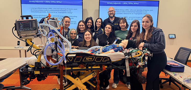 A group of people surround a gurney with a manikin on it.