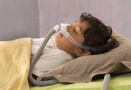 A child in bed wears a CPAP