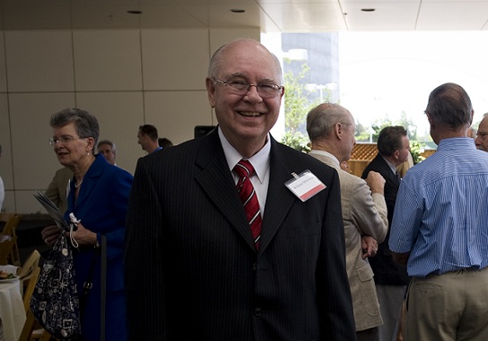 William McGowan stands at a UC Davis Health event wearing a dark suit and red striped tie while attendees gather in the background.