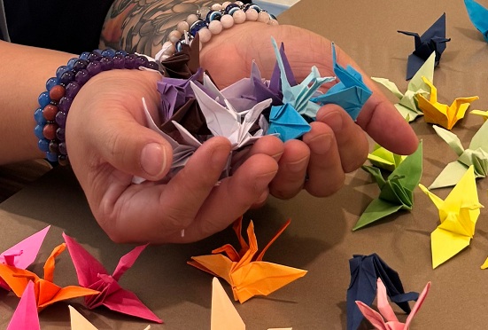 Staff member holds several colorful origami cranes while dozens of folded paper cranes.