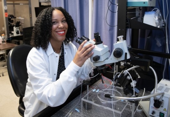 Researcher Theanne Griffith sits using a microscope-like instrument surrounded by scientific equipment.
