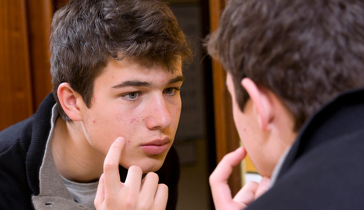 teen boy looking at his face in the mirror