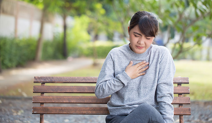 woman holding her chest on a park bench