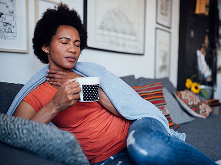 woman sick on the couch holding a cup