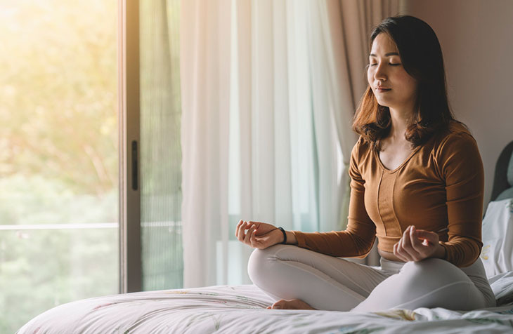 woman meditating while sitting on her bed