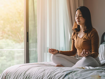 woman meditating while sitting on her bed