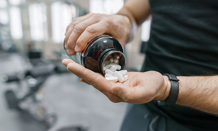 man pouring out bottle of athletic supplement pills