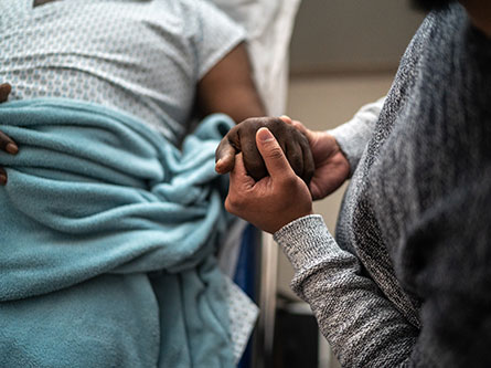person in hospital bed holding hands with visitor