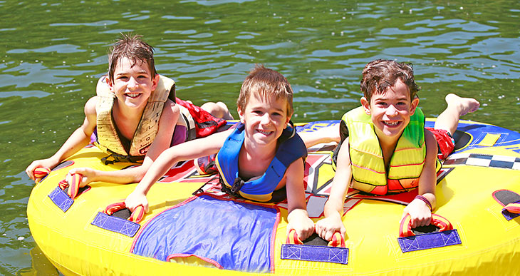 kids wearing life jackets on an inner tube in a lake