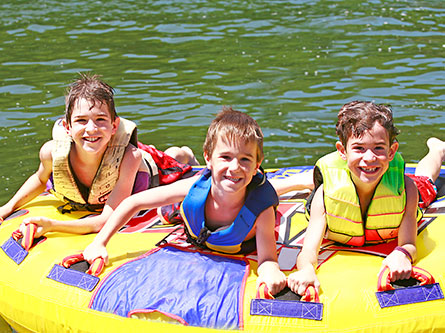 kids wearing life jackets on an inner tube in a lake