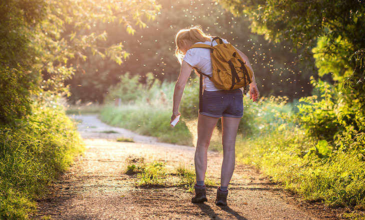 woman spraying mosquito repellent while walking on trail