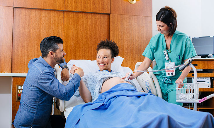 pregnant mother in hospital bed next to father and nurse