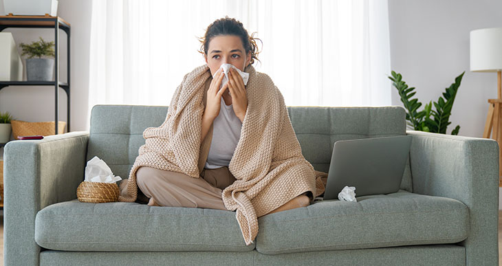 woman blowing her nose sitting on a couch
