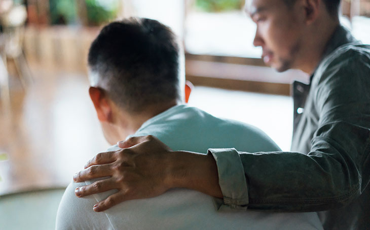 man with his arm around another man to comfort him