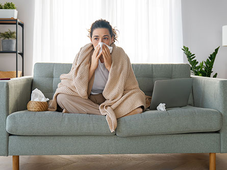 woman blowing her nose sitting on a couch