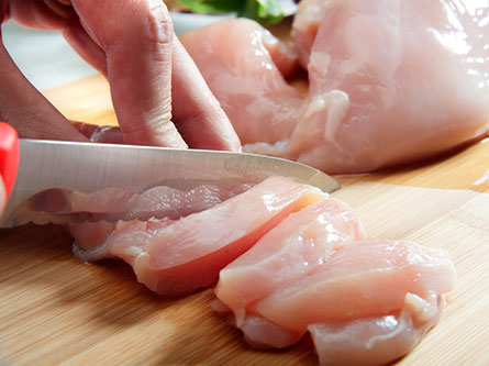 person cutting raw chicken on a cutting board