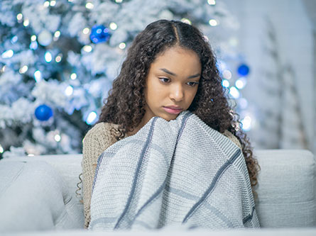 woman wrapped in a blanket on a couch with a Christmas tree behind her