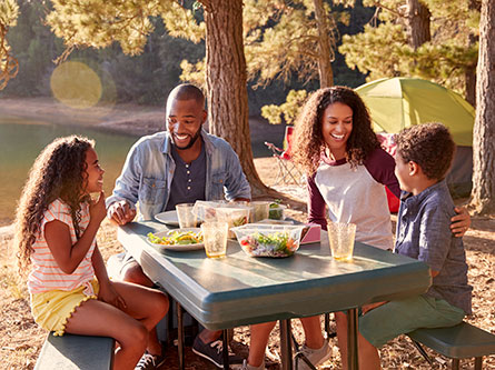 Family of four eating at a table at a campsite outdoors