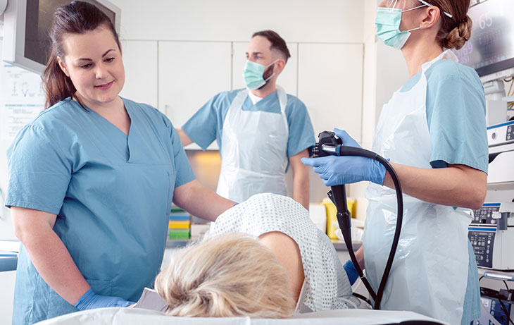 Three health care providers performing colonoscopy on woman laying on a table