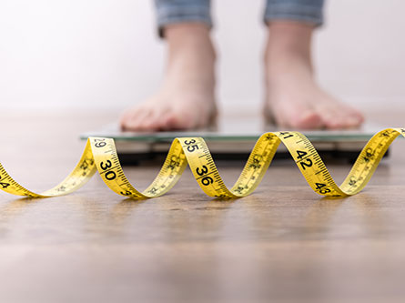 person standing on a scale with a measuring tape in front for weight loss medications