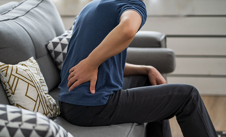 man sitting on a couch holding his lower back in pain from kidney stones