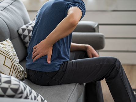 man sitting on a couch holding his lower back in pain from kidney stones