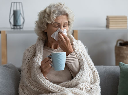 older woman coughing and blowing her nose with pneumonia symptoms