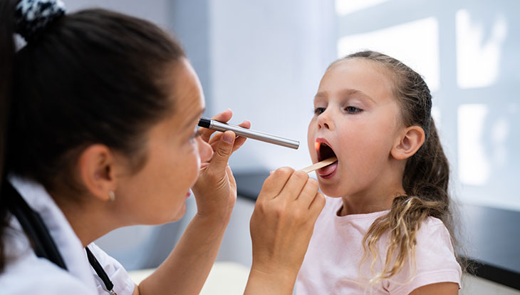 female health care provider checking girl's throat for strep throat or sore throat