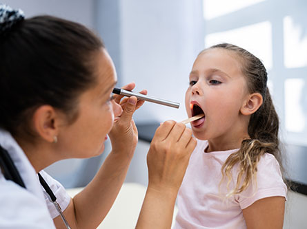 female health care provider checking girl's throat for strep throat or sore throat