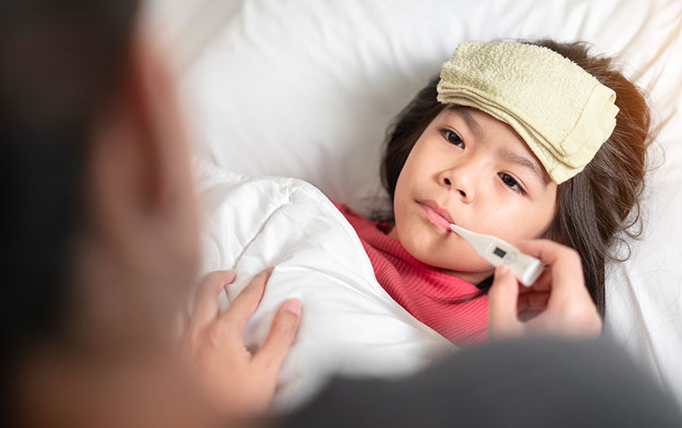 young child in bed with a thermometer as parent is concerned about fever