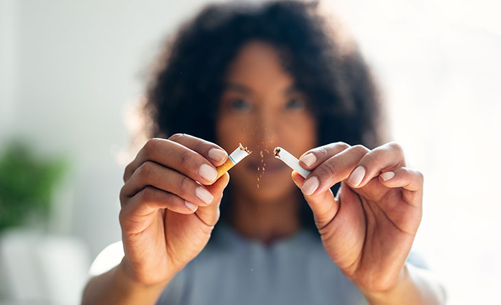 woman breaking cigarette in half as she quits smoking for health benefits