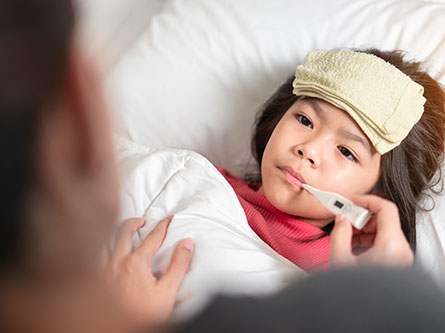 young child in bed with a thermometer as parent is concerned about fever