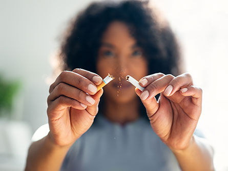 woman breaking cigarette in half as she quits smoking for health benefits