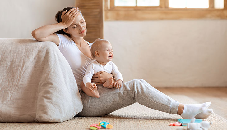 woman looking stressed sitting with her baby in her lap possibly suffering postpartum psychosis
