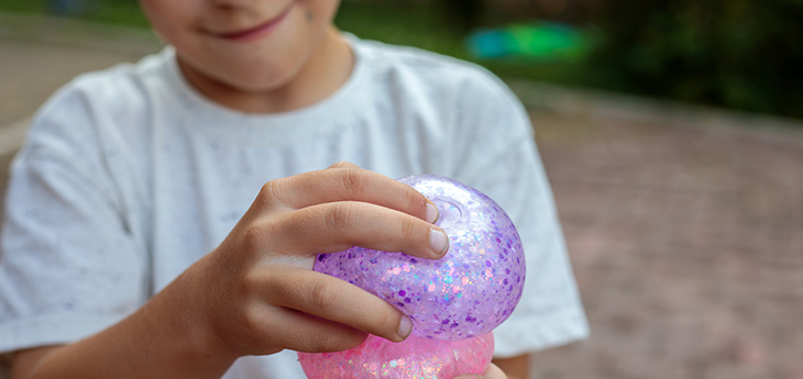A young boy plays with a purple and pink, glittery squishy toy.