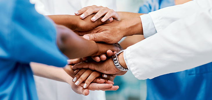 Diverse group of healthcare providers&rsquo; hands stacked together.