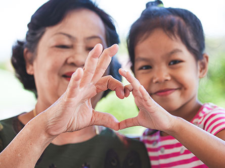 older woman and young girl making a heart with their hands