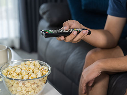 person with a TV remote and a bowl of popcorn
