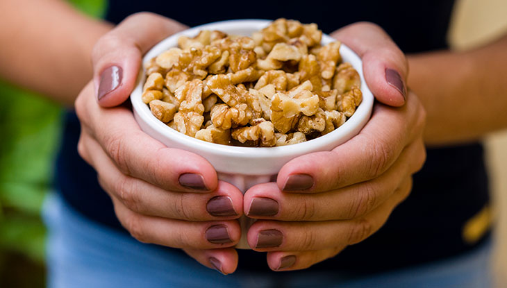 two hands holding a bowl of walnuts