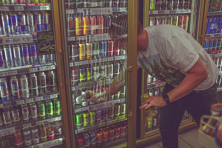 man reaching for energy drinks in a store refrigerator