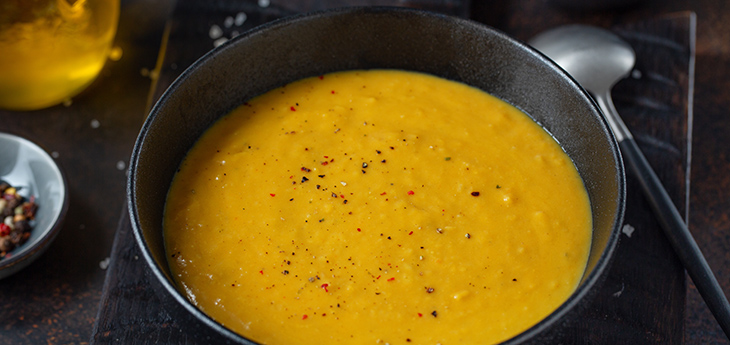 Bowl of winter squash lentil soup sprinkled with pepper flakes, in a dark bowl with a spoon.