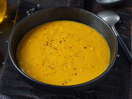 Bowl of winter squash lentil soup sprinkled with pepper flakes, in a dark bowl with a spoon.