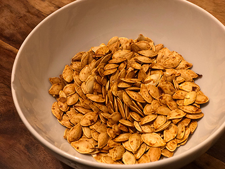 Roasted, seasoned squash seeds in a white bowl made for crunchy snack.